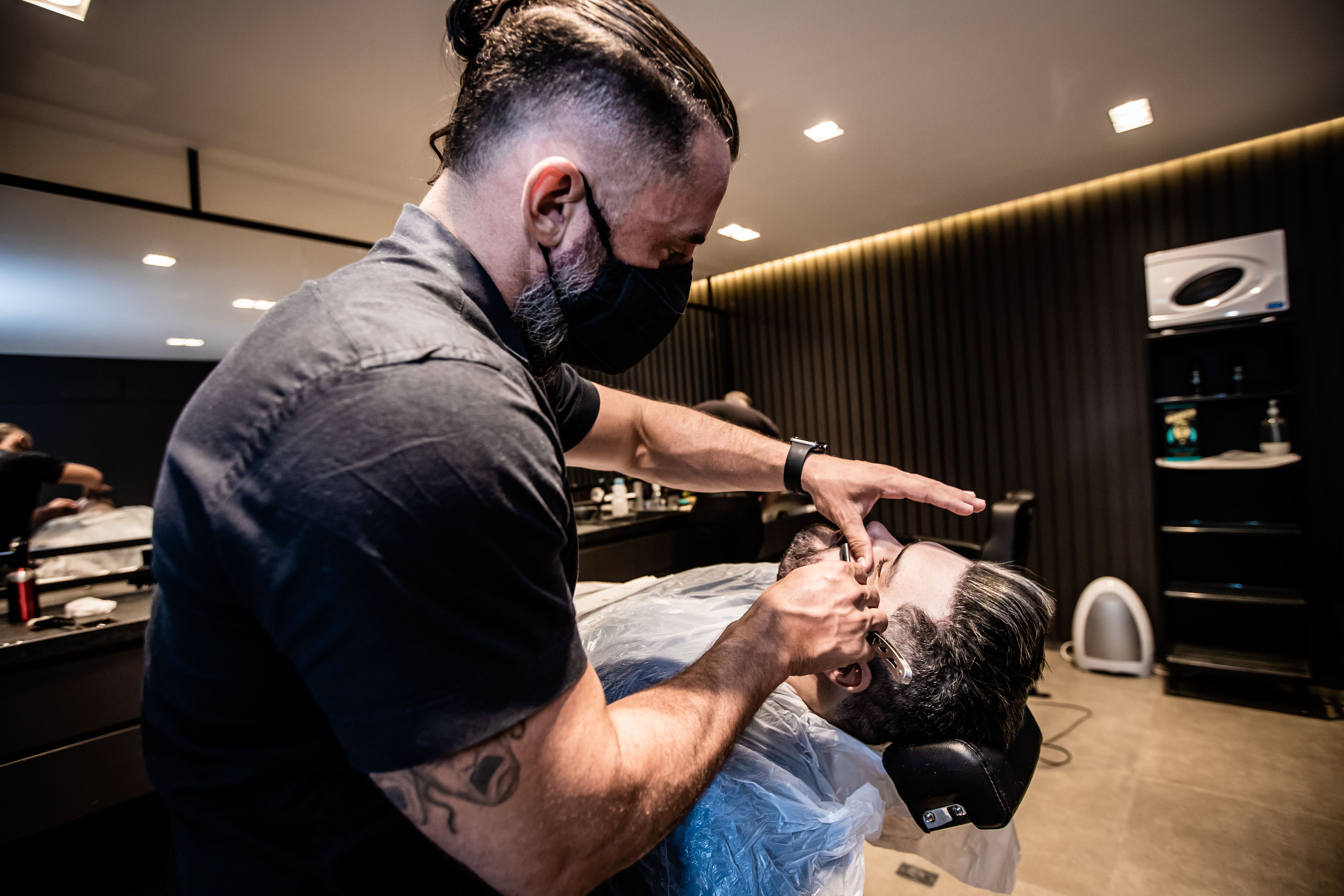 Dono de barbearia organizando produtos como pomadas e óleos em uma prateleira.